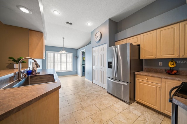 kitchen featuring stainless steel refrigerator with ice dispenser, electric range, light brown cabinets, a sink, and a textured ceiling