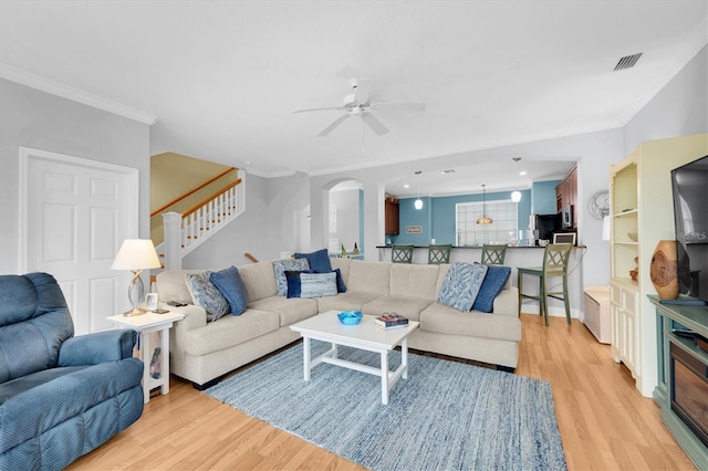 living room featuring ornamental molding, arched walkways, stairway, and light wood finished floors