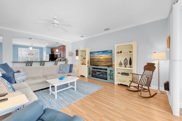 living room with light wood finished floors, visible vents, a ceiling fan, a glass covered fireplace, and crown molding