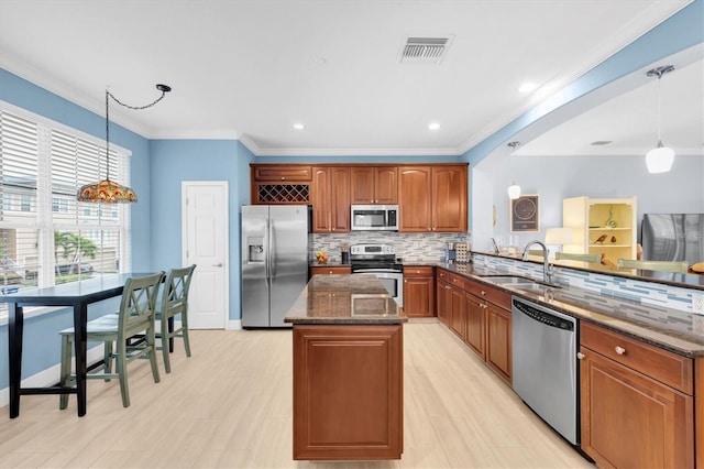 kitchen featuring stainless steel appliances, a peninsula, a sink, ornamental molding, and dark stone counters