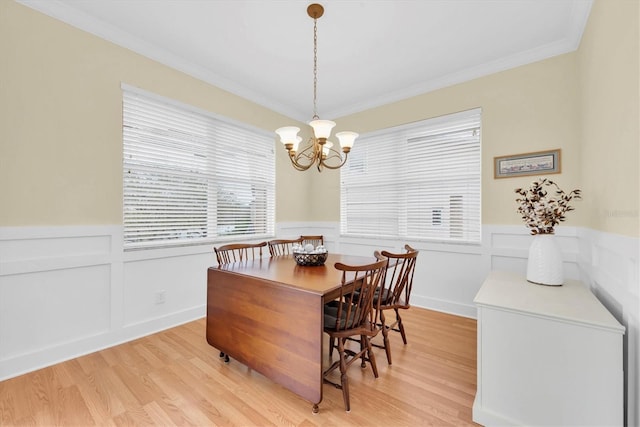 dining space with light wood-style floors, a chandelier, wainscoting, and crown molding