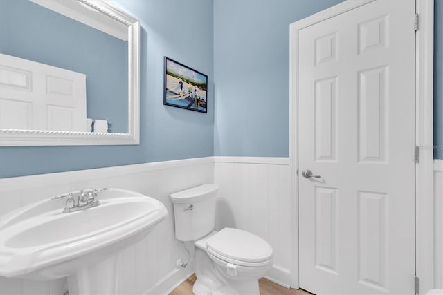 half bath with toilet, a wainscoted wall, a sink, and wood finished floors