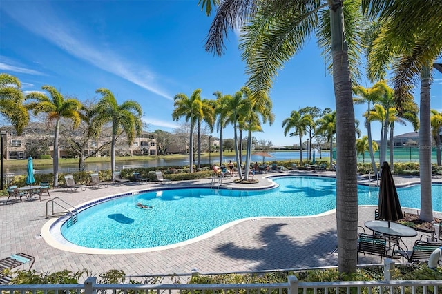 community pool with a water view, fence, and a patio