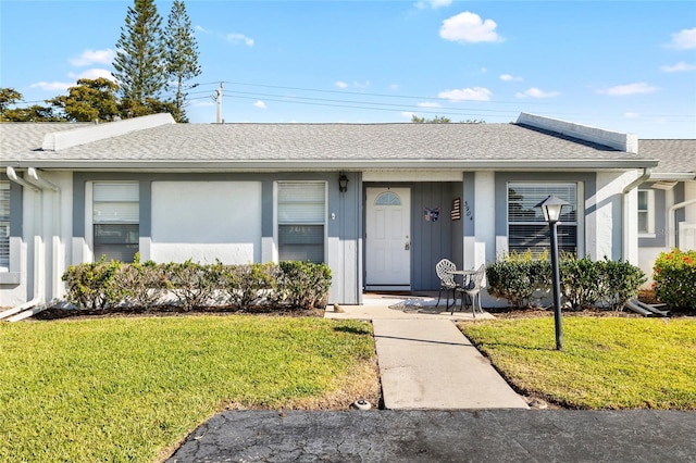 ranch-style home with stucco siding, roof with shingles, and a front yard