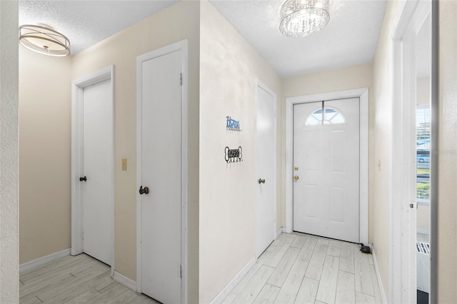 foyer with light wood-style flooring, baseboards, a chandelier, and a textured ceiling