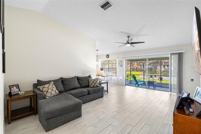 living area featuring light wood finished floors, visible vents, lofted ceiling, and a ceiling fan