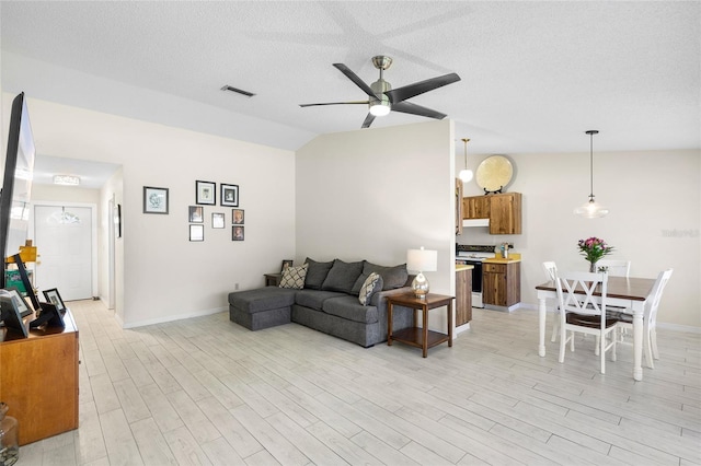 living room featuring visible vents, lofted ceiling, ceiling fan, light wood-style floors, and a textured ceiling