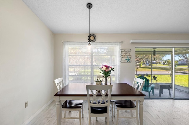 dining area featuring light wood-style floors, baseboards, and a textured ceiling