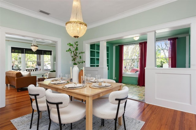 dining space featuring crown molding, a notable chandelier, wood finished floors, and visible vents