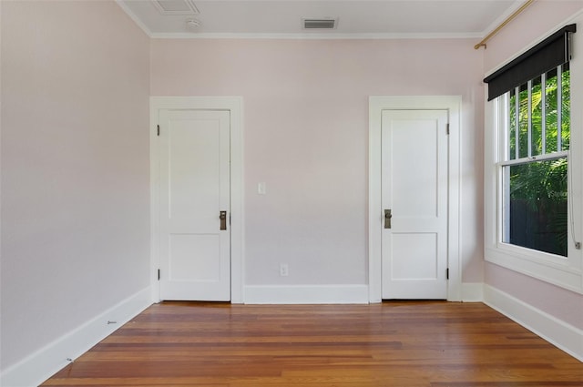 empty room featuring crown molding, wood finished floors, visible vents, and baseboards