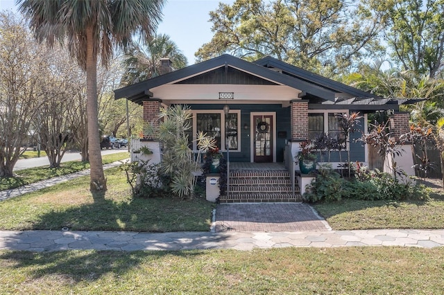 view of front of home with a porch, brick siding, a front yard, and a chimney