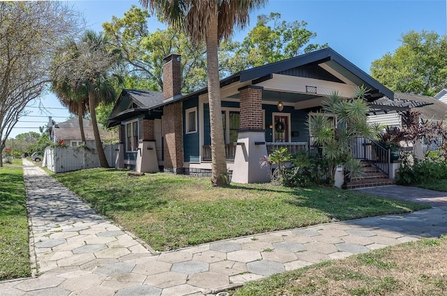 view of front of property featuring brick siding, a porch, a chimney, and a front yard