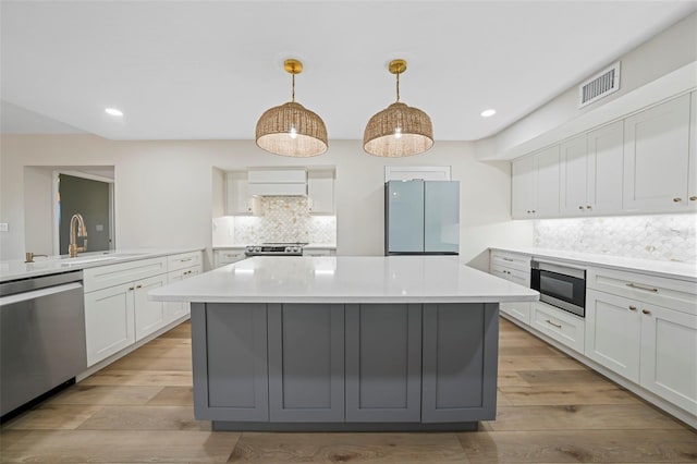 kitchen with visible vents, a sink, a kitchen island, stainless steel appliances, and light countertops