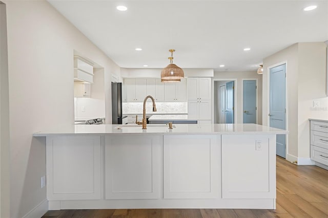 kitchen featuring backsplash, light countertops, freestanding refrigerator, wood finished floors, and a sink