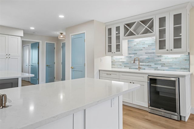 kitchen featuring a sink, backsplash, white cabinetry, wine cooler, and light wood-style floors