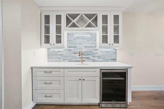 bar featuring baseboards, wet bar, a sink, wine cooler, and tasteful backsplash