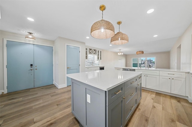 kitchen featuring gray cabinets, a center island, white cabinetry, light wood-style floors, and light countertops