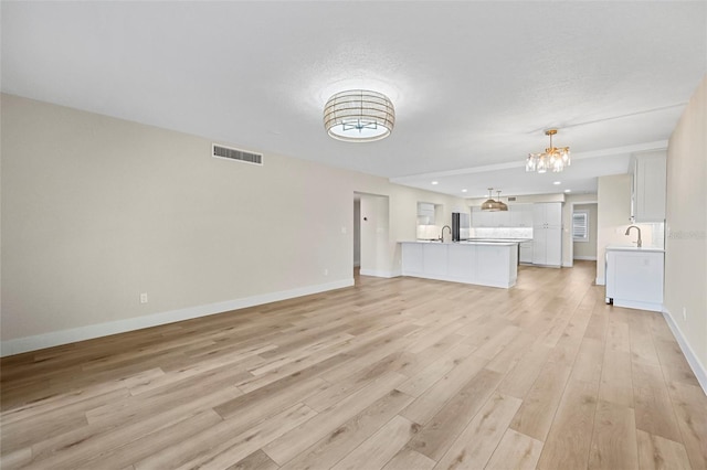 unfurnished living room featuring light wood finished floors, visible vents, baseboards, an inviting chandelier, and a sink