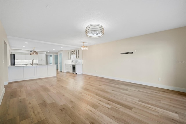 unfurnished living room featuring light wood-type flooring, a notable chandelier, a sink, recessed lighting, and baseboards