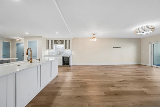 kitchen with tasteful backsplash, beverage cooler, light countertops, light wood-style flooring, and white cabinets