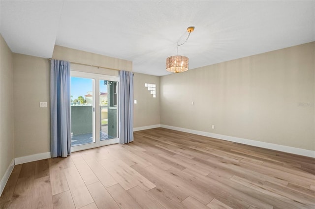 spare room with a notable chandelier, light wood-type flooring, and baseboards