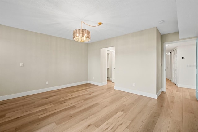 spare room with light wood-style flooring, baseboards, and a chandelier