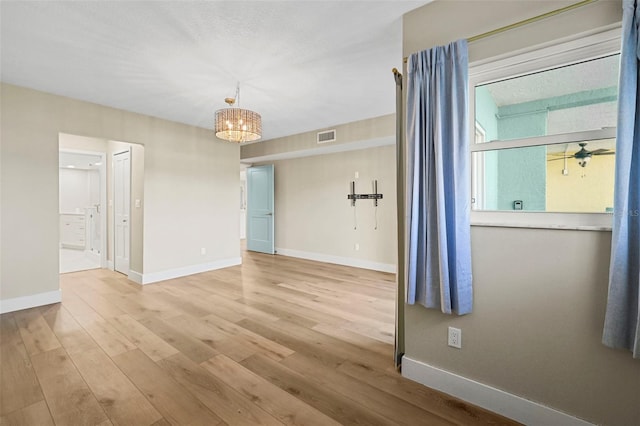 spare room featuring ceiling fan with notable chandelier, light wood-style floors, visible vents, and baseboards