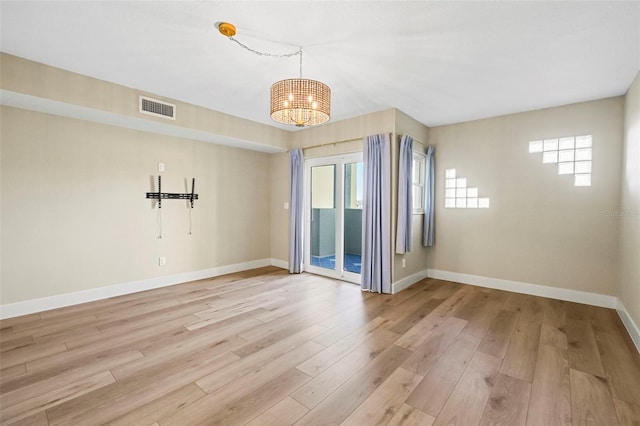 unfurnished room with an inviting chandelier, light wood-style floors, visible vents, and baseboards