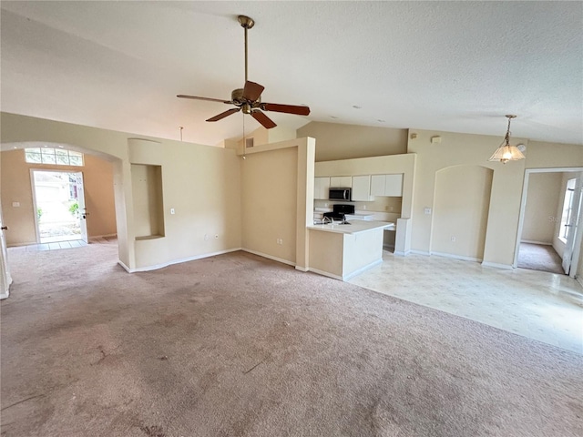 unfurnished living room with arched walkways, light colored carpet, ceiling fan, vaulted ceiling, and a textured ceiling