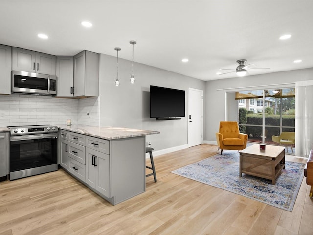 kitchen with gray cabinetry, a peninsula, appliances with stainless steel finishes, decorative backsplash, and light wood finished floors