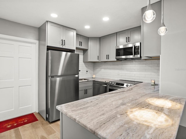 kitchen featuring light stone countertops, light wood-style flooring, appliances with stainless steel finishes, and gray cabinets