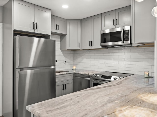 kitchen with light stone counters, recessed lighting, backsplash, gray cabinetry, and appliances with stainless steel finishes