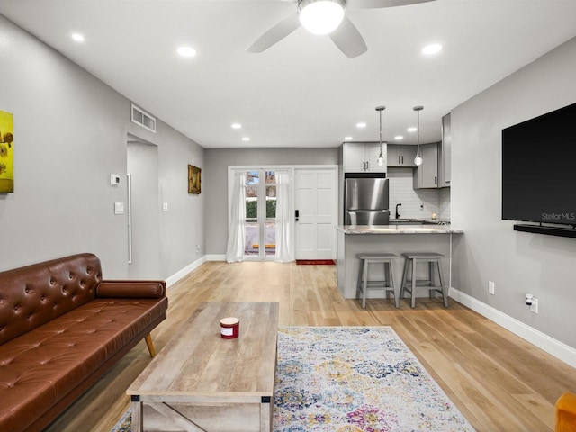 living area featuring ceiling fan, light wood-type flooring, visible vents, and baseboards