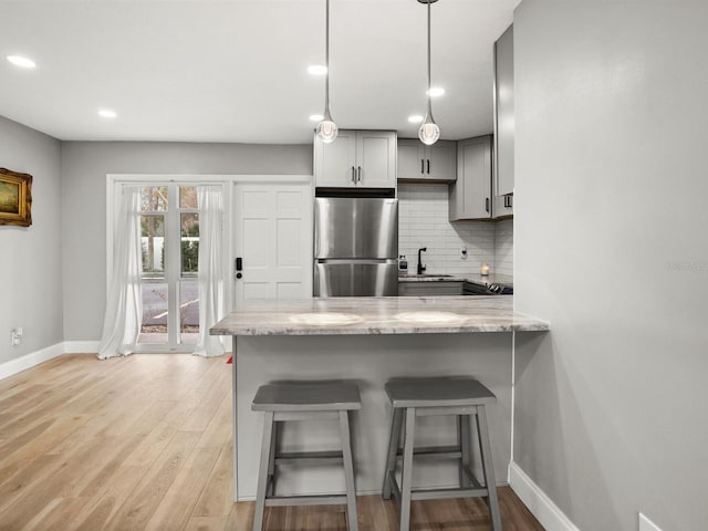 kitchen featuring light stone counters, freestanding refrigerator, gray cabinets, and backsplash