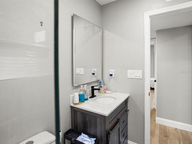 ensuite bathroom featuring connected bathroom, baseboards, wood finished floors, and vanity