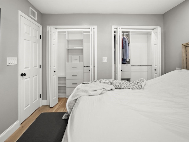 bedroom with light wood-type flooring, two closets, visible vents, and baseboards