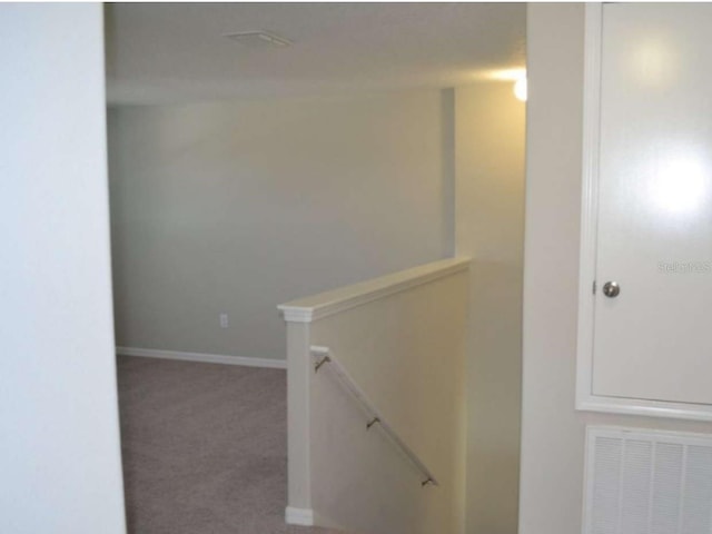 hallway featuring an upstairs landing, visible vents, carpet flooring, and baseboards