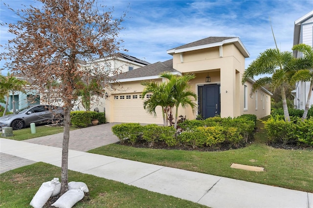 view of front of house with a shingled roof, an attached garage, decorative driveway, a front lawn, and stucco siding