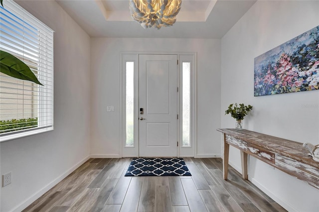 foyer entrance featuring a raised ceiling, a notable chandelier, baseboards, and wood finished floors