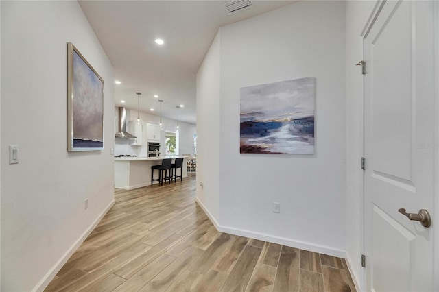 hallway with light wood finished floors, baseboards, visible vents, and recessed lighting