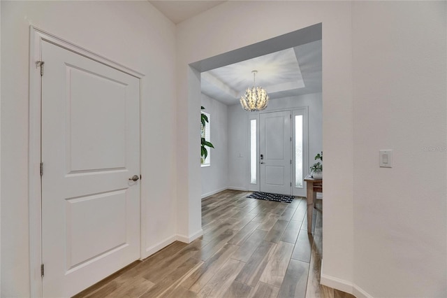 foyer entrance featuring light wood-type flooring, baseboards, a notable chandelier, and a tray ceiling