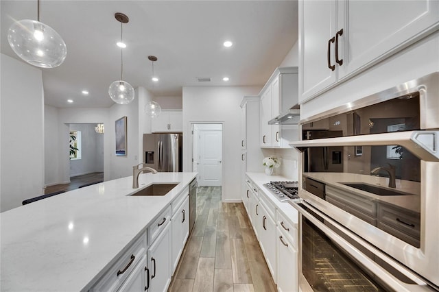 kitchen with decorative light fixtures, light wood finished floors, appliances with stainless steel finishes, white cabinets, and a sink