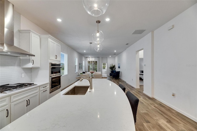 kitchen with stainless steel appliances, tasteful backsplash, white cabinetry, a sink, and wall chimney exhaust hood