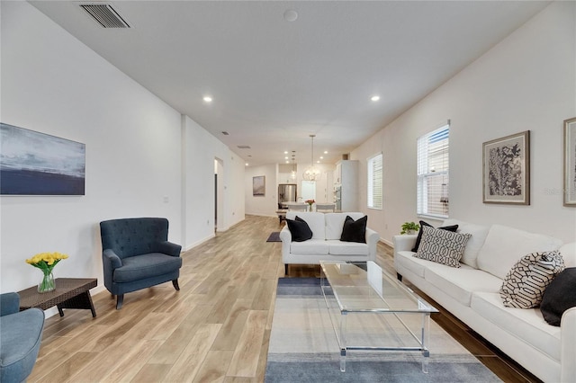 living area featuring light wood-style floors, recessed lighting, visible vents, and an inviting chandelier