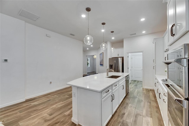 kitchen featuring an island with sink, stainless steel appliances, light countertops, light wood-type flooring, and a sink