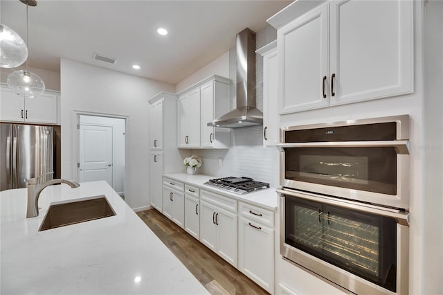 kitchen featuring dark wood finished floors, stainless steel appliances, wall chimney range hood, white cabinetry, and a sink