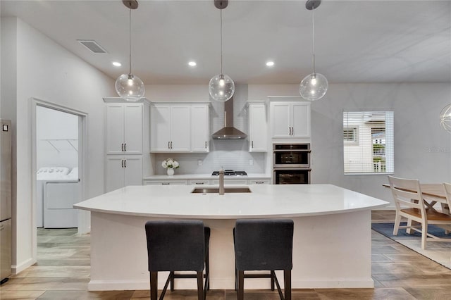 kitchen featuring decorative backsplash, wall chimney exhaust hood, appliances with stainless steel finishes, light countertops, and a sink