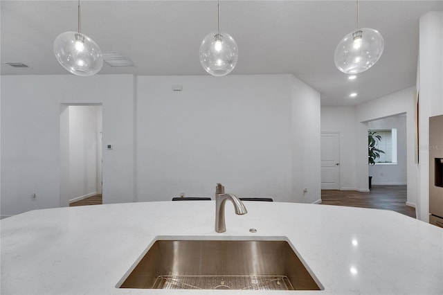 kitchen with wood finished floors, a sink, visible vents, light stone countertops, and pendant lighting