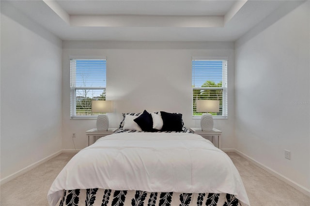 bedroom with a tray ceiling, multiple windows, and baseboards