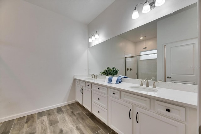 bathroom with wood finished floors, a sink, a shower stall, and double vanity